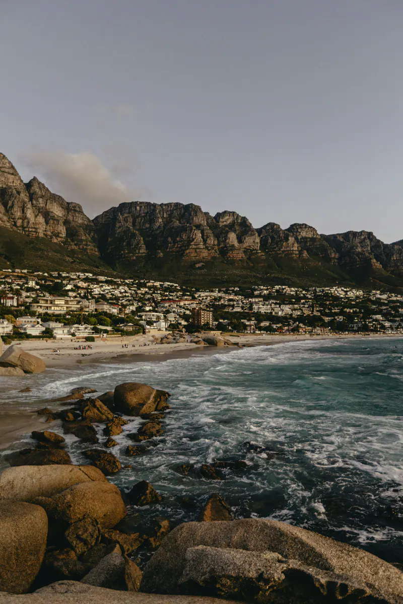 Waves over rocks at dusk, with a seaside town below a mountain ridge