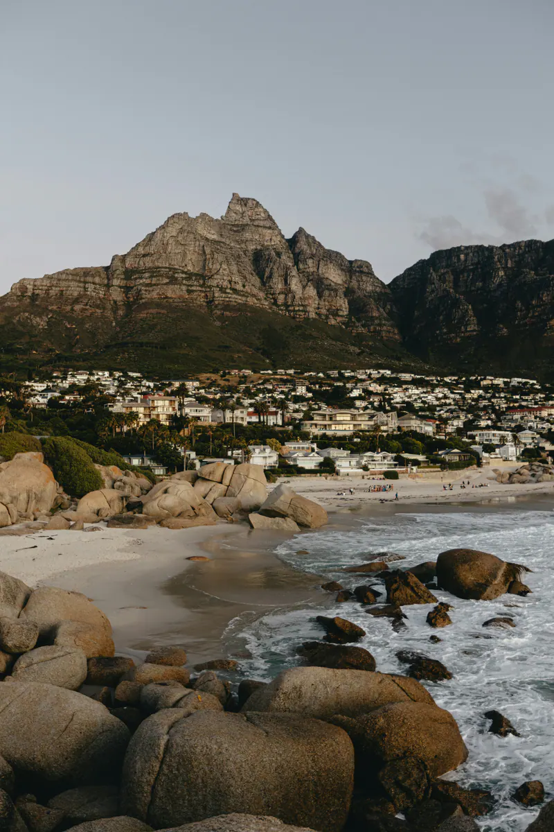 A small beach between boulders, with houses on the slope under a rocky peak