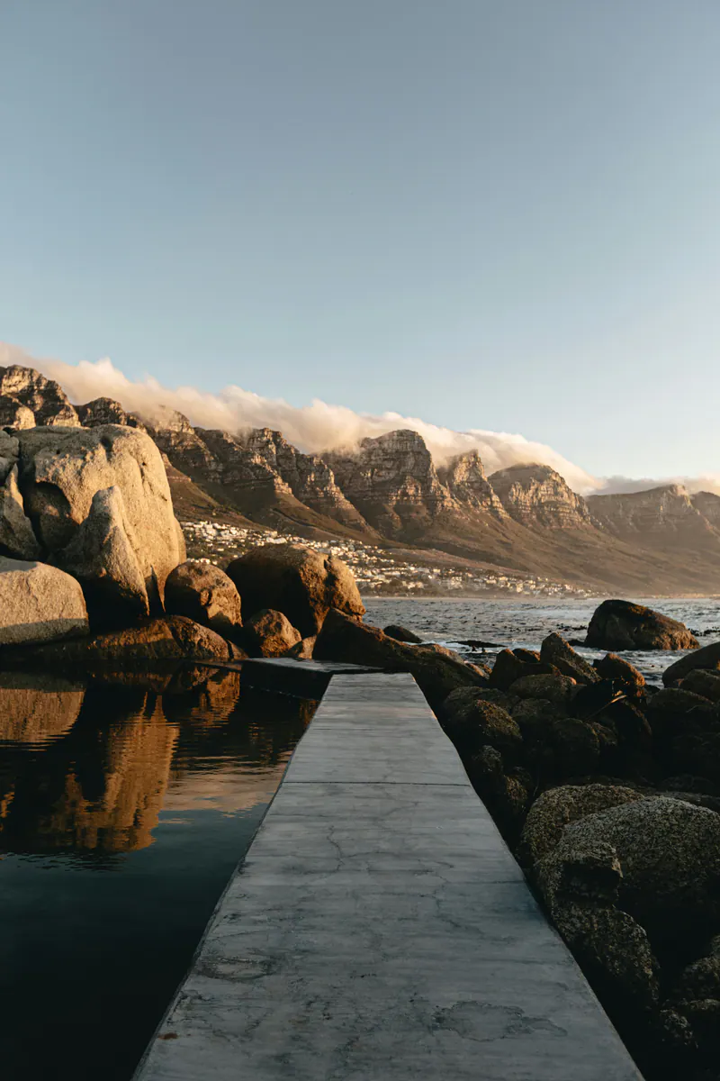 A concrete walkway beside a tidal pool, with boulders and mountains beyond