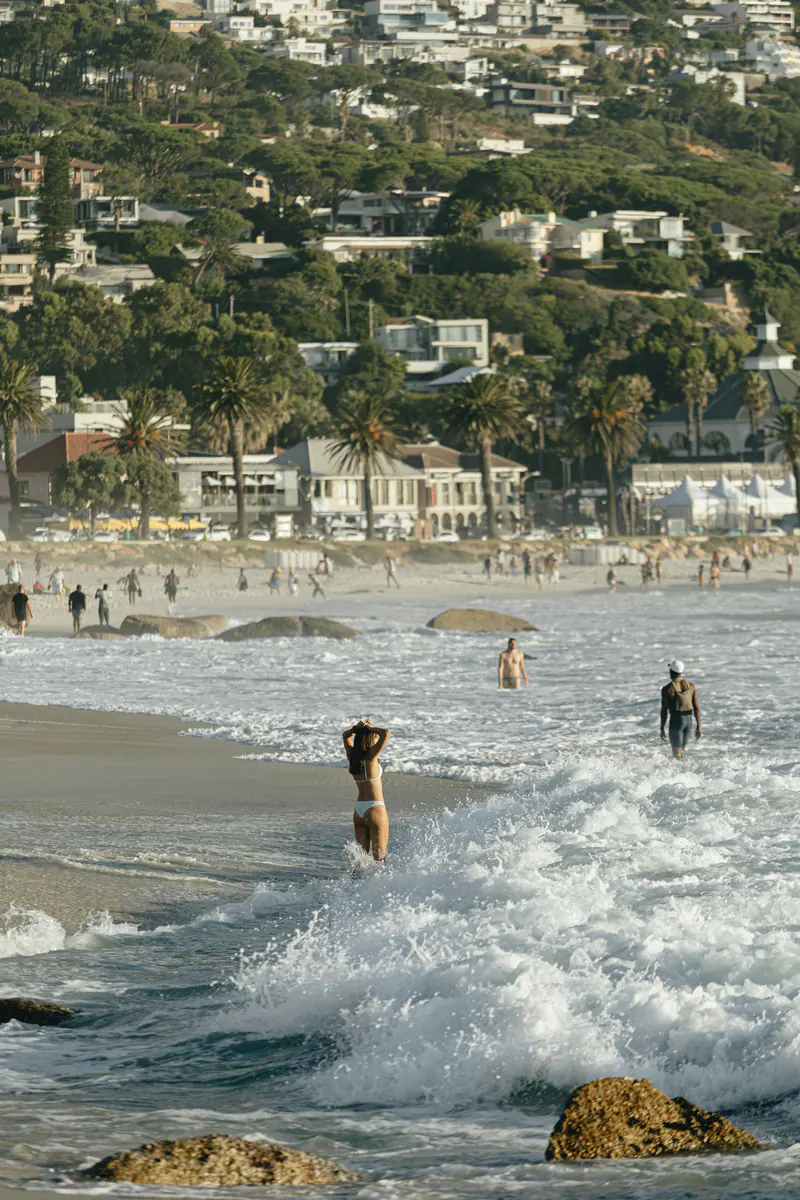 Swimmers in the surf at a busy beach, houses climbing the hill behind