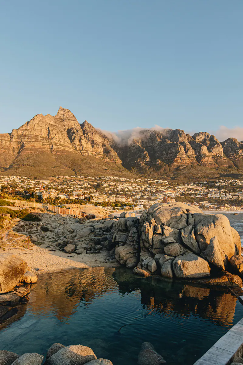 Boulders reflected in a still tidal pool, with the mountains glowing at sunset