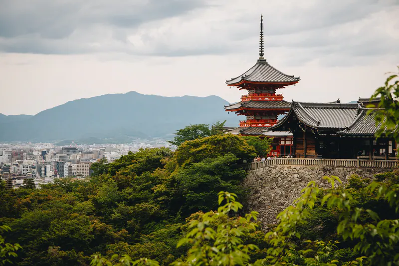 A red pagoda on a wooded hillside, with Kyoto and the mountains beyond