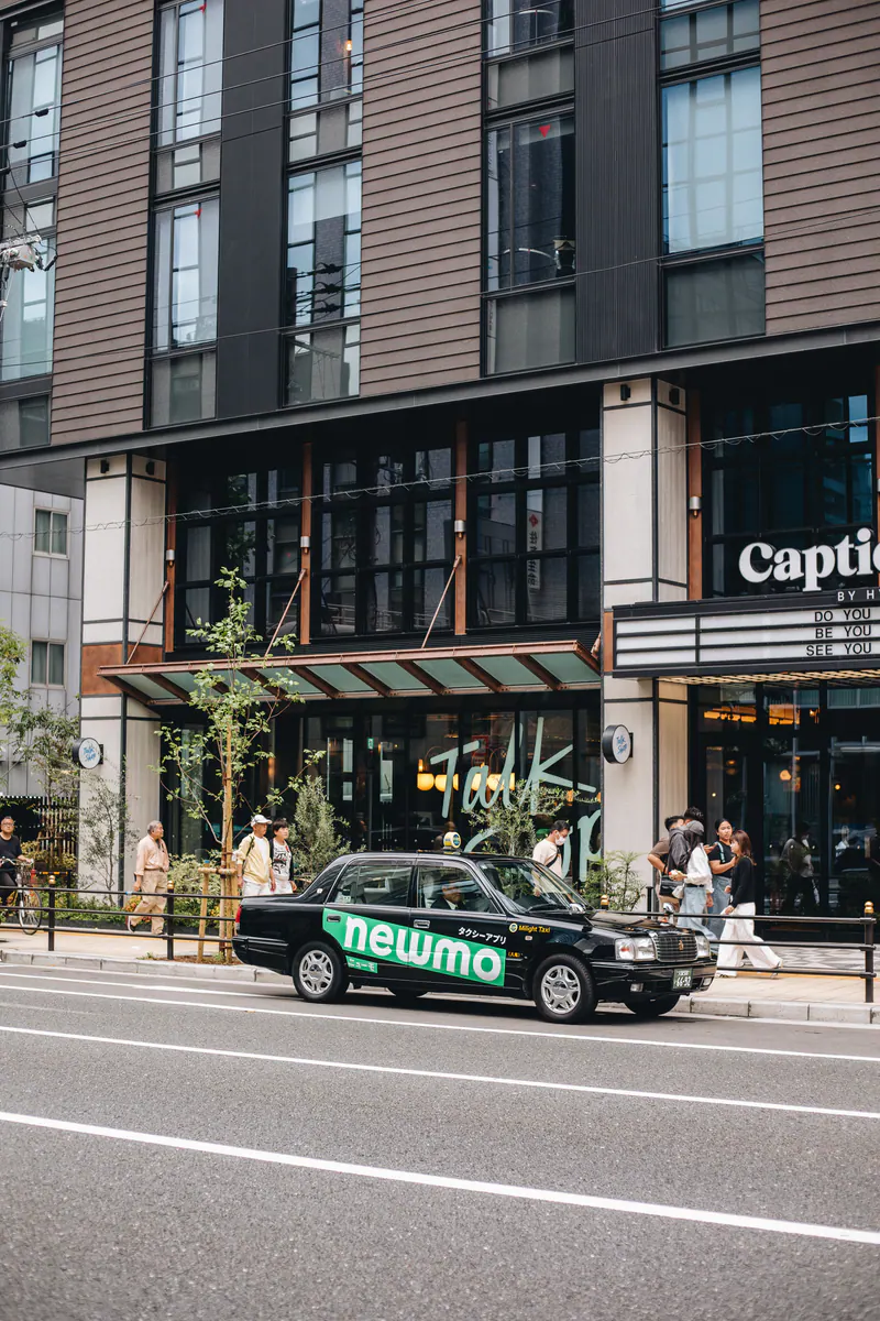 A black taxi passing a modern building with shops at street level