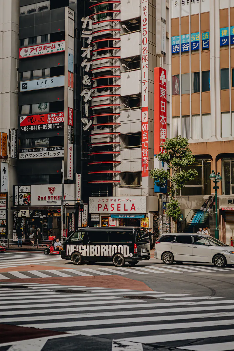 A van on a striped crossing in Tokyo, under tall buildings covered in signs