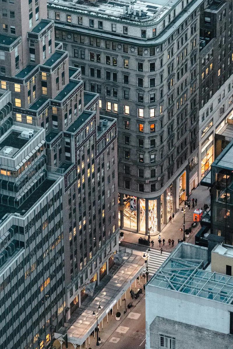 A grey office block with lit shop windows on its corner, seen from above
