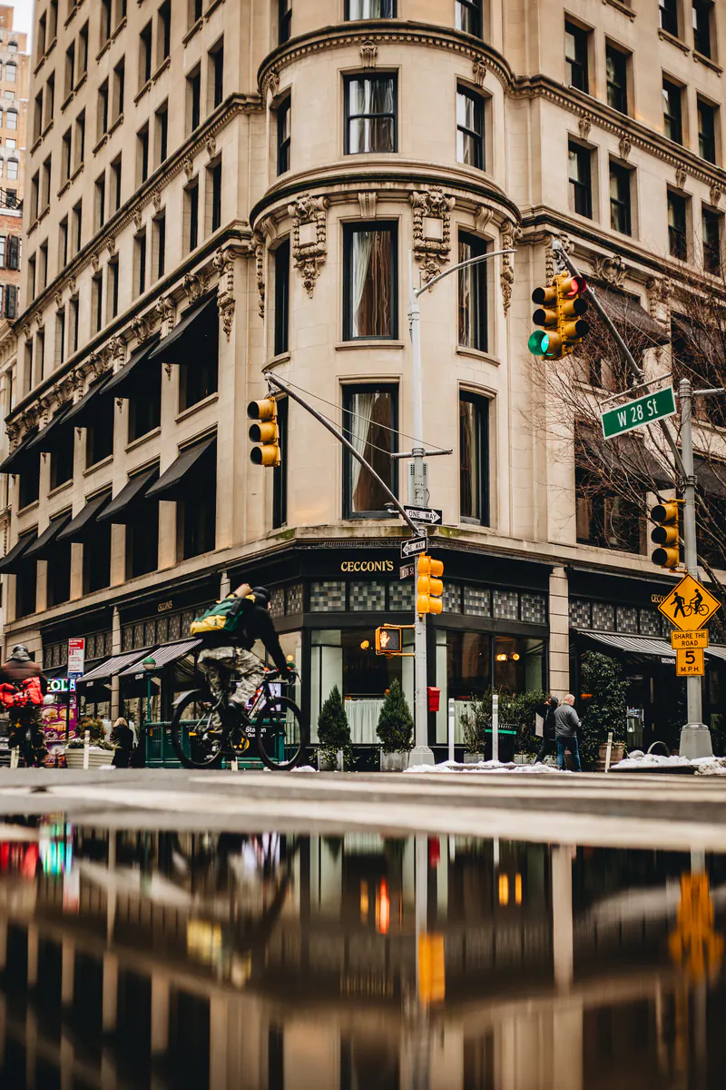 A corner building and a cyclist reflected in a puddle