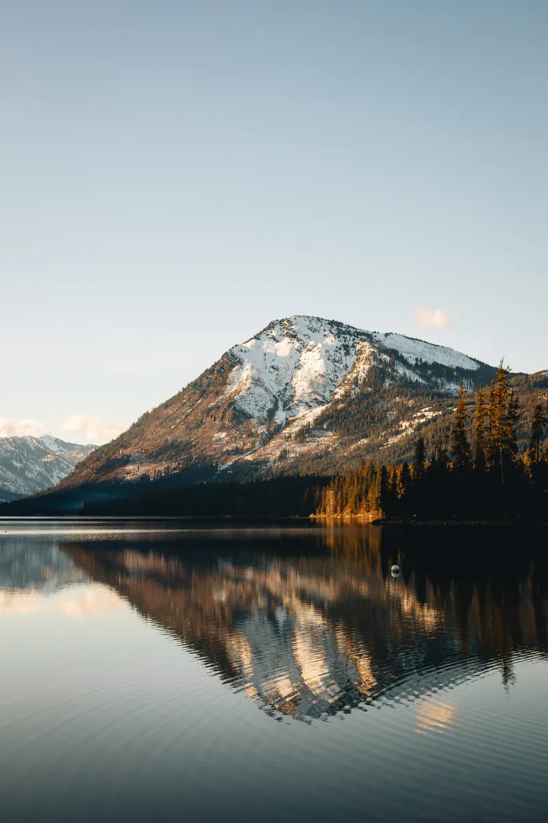 A snowy peak and golden trees reflected in rippled water