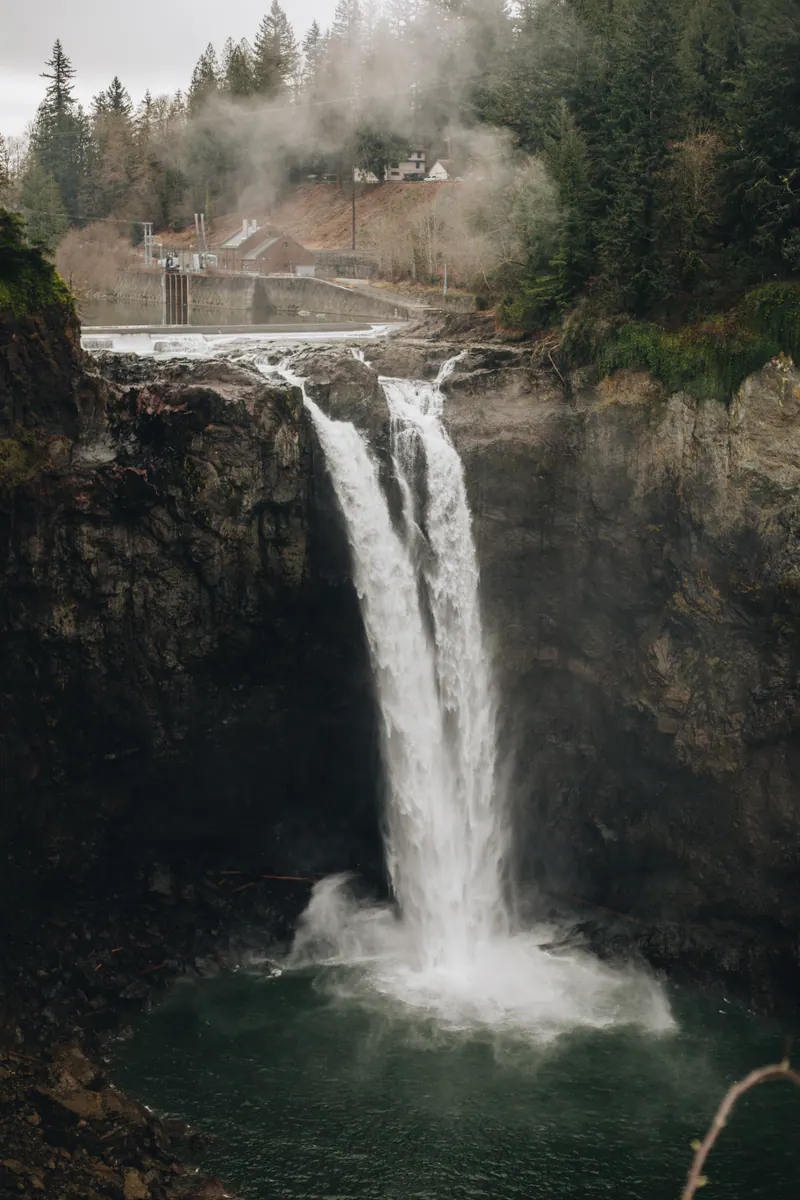 A waterfall dropping into a misty gorge, with a lodge on the cliff above